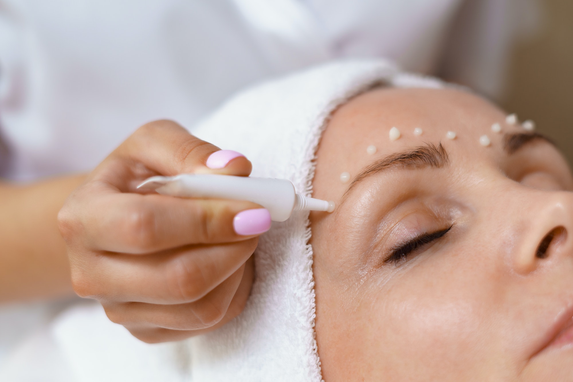 Cosmetologist applying cream on face