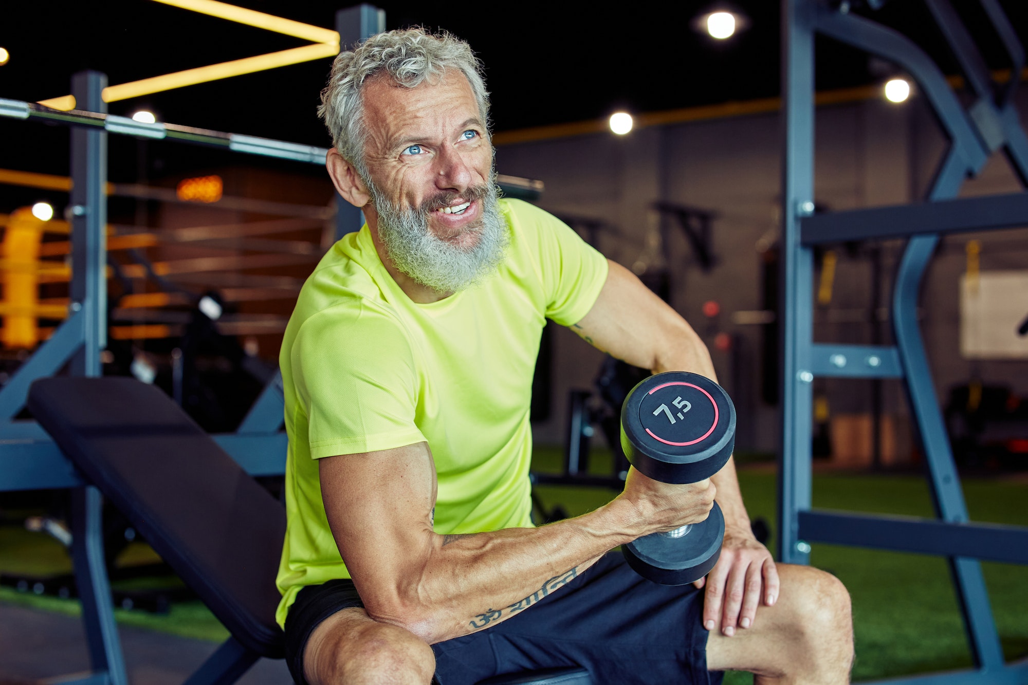 Portrait of a strong mature man in sportswear lifting heavy dumbbells and pumping his biceps