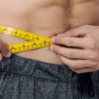 panoramic shot of shirtless man measuring waist
